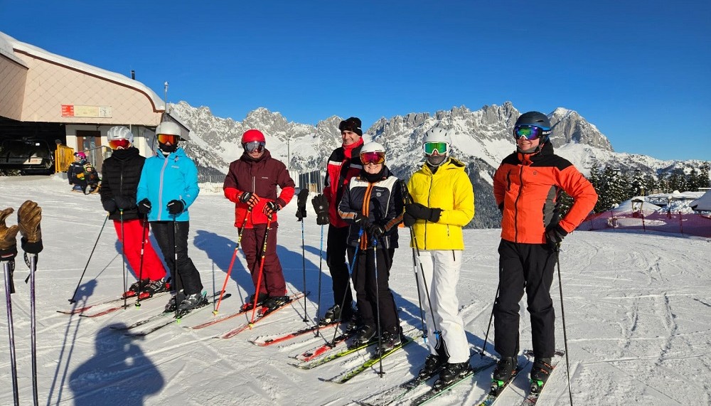 Eine Gruppe Hotelgäste genießt den gemeinsamen Skitag mit Hotelchef Hans 
